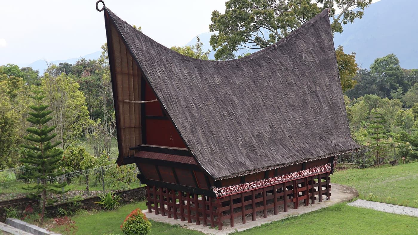 A traditional Batak house with a sweeping saddle roof on carved wooden pillars