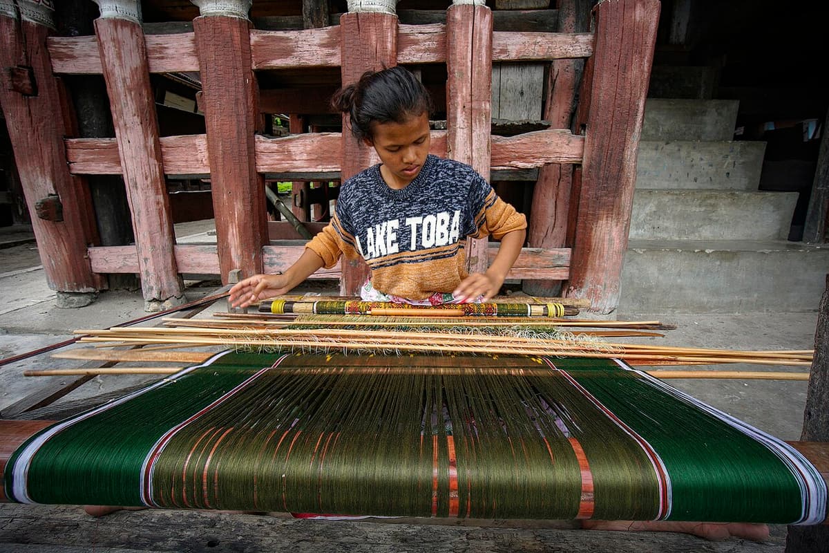 A weaver working on an ulos cloth at a loom